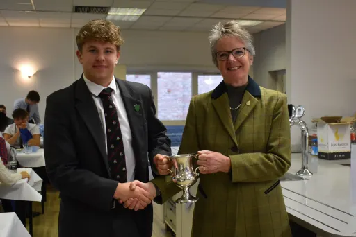 lady and boy stand shaking hands and holding a trophy cup a