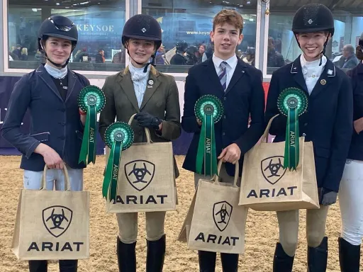 four Pocklington School equestrian team members wearing riding apparel and holding ARIAT bags and rosettes