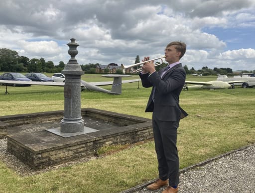 Youth playing trumpet, stood in front of war memorial at Wolds Gliding Club