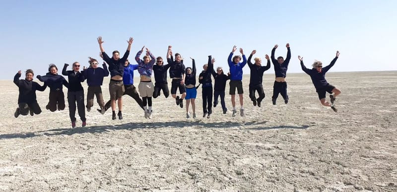 16 teenagers jumping in a line outside