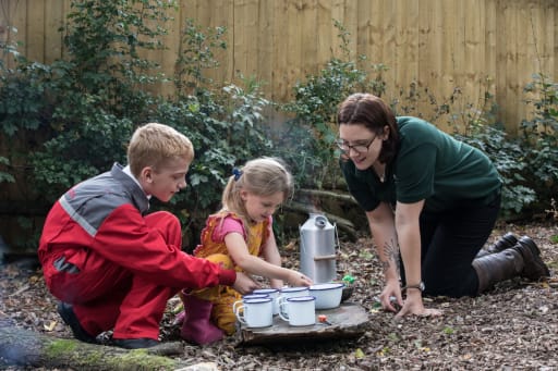 Girl and boy making tea outside with forest school practitioner