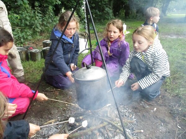 Four Prep School pupils sit round a camp fire, toasting marshmellows