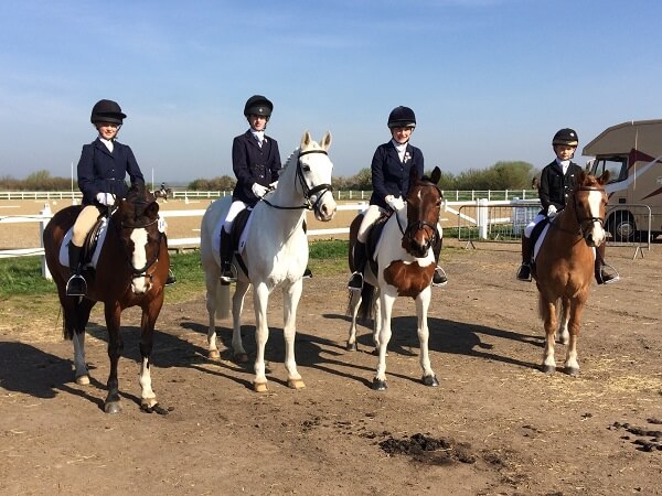 Four riders and horses of the Pocklington School Dressage team, stand in the paddock at the NSEA National County Championships