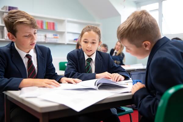 Three Pocklington School pupils working together at a desk in a classroom.