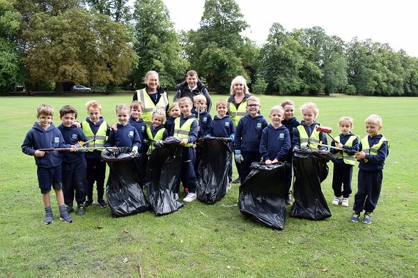 Pocklington Prep School children and teachers hold litter picking equipment in a public park.