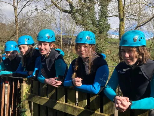 Pupils wearing wet suits and blue helmets, leaning over a fence