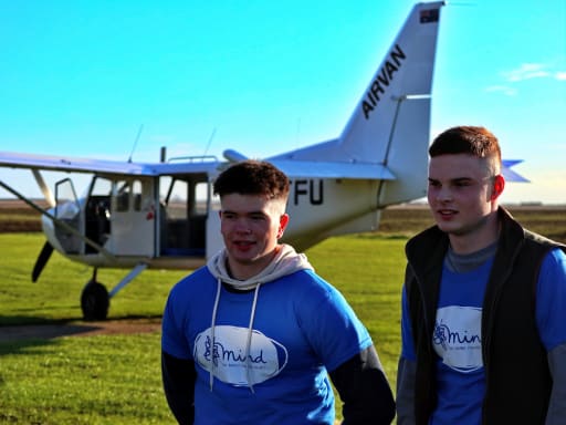 Two boys stood in front of skydive aeroplane, wearing t-shirts with the MIND charity logo