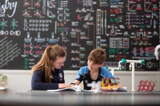 2 pupils sat reading a book in a school science lab