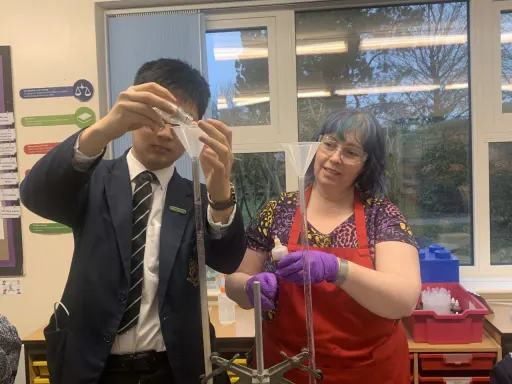 Lab Technician watching pupil using science apparatus in a classroom laboratory