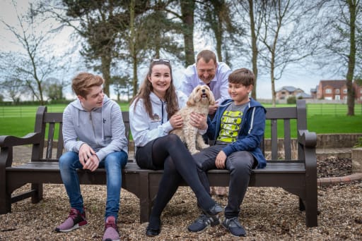 3 boarding pupils and staff member sat on bench with dog, in campus grounds