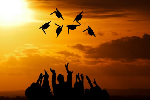 silhouette of people throwing graduation caps into the air