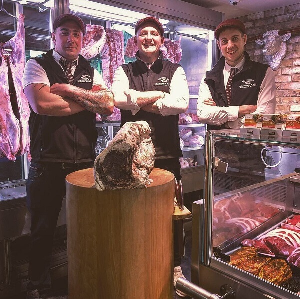 Three butchers stand in front of a beef steak on a butchers block in the Pocklington branch of A Laverack & Son.