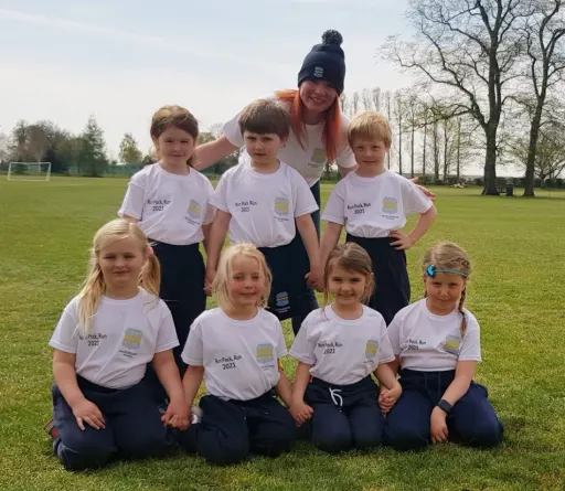 Group of children and teacher sat on school field wearing Run Pock Run shirts and bobble hat