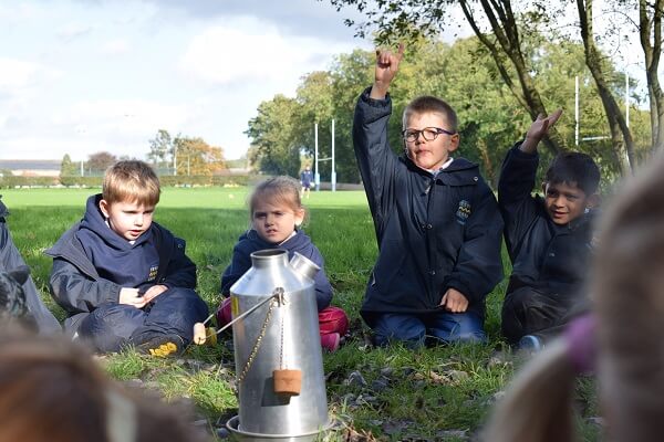 Children sit on school field for a Forest School lesson