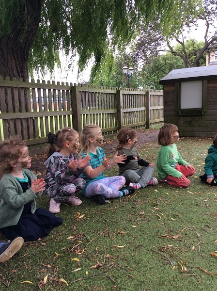 Pre-School children sat on a grass lawn, wearing camouflage clothing and face paint