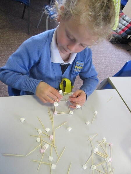 Girl sat at table making a 3D construction with marshmellows and cocktail sticks