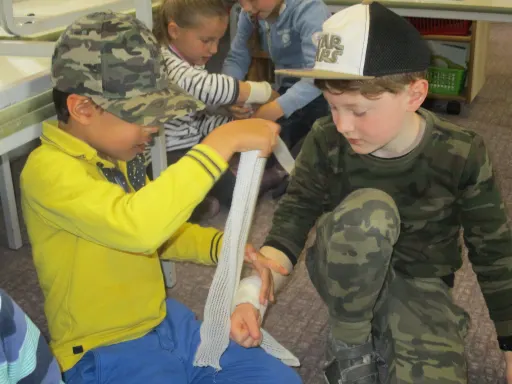 two boys practicing bandaging as part of first aid in a classroom