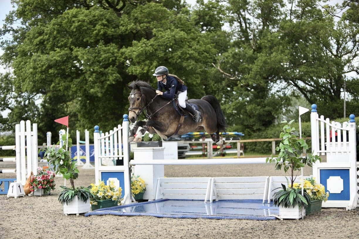 rider and pony jumping over showjumping fence in a showjumping arena