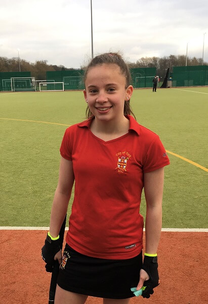 girl wearing City of York Hockey Club colours and holding a hockey stick, stood on an a hockey astro pitch