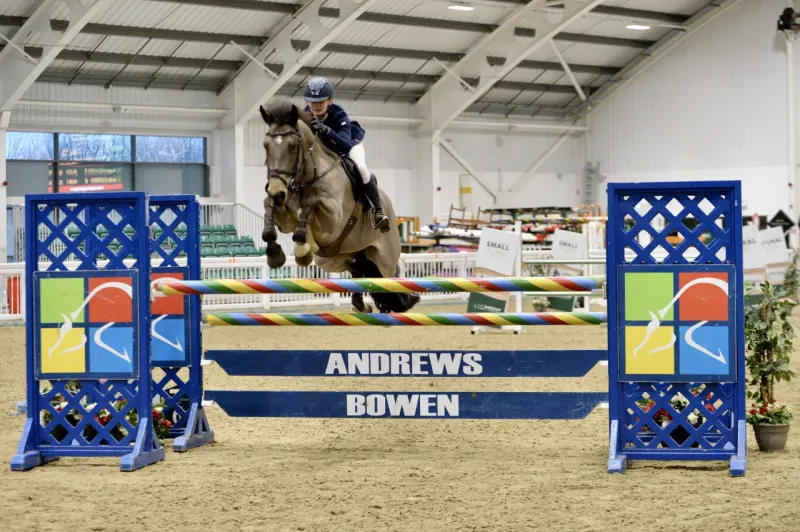 rider and pony jumping a fence in a showjumping competition in an equestrian arena