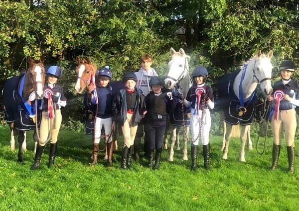 Pocklington School riders and horses with their rosettes, in a field at the NSEA Championships