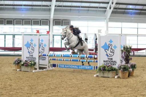 Rider and pony mid-jump at the  British Showjumping Indoor Championships