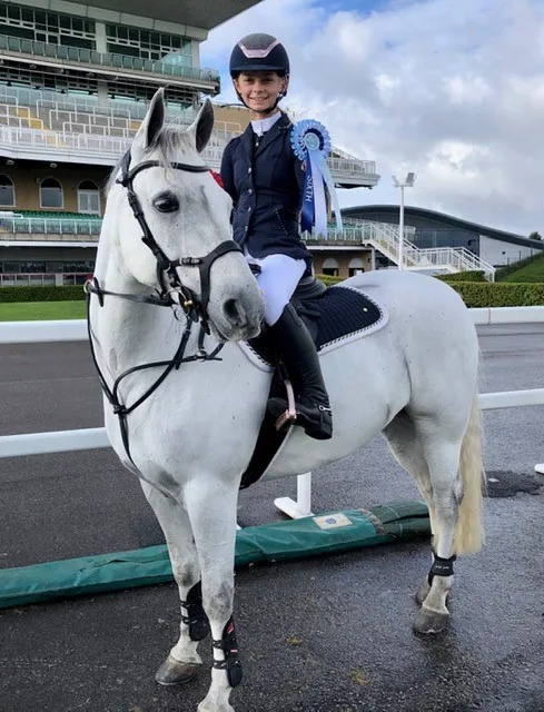 Rider sat on white pony holding a blue rosette at the Aintree Equestrian  Centre