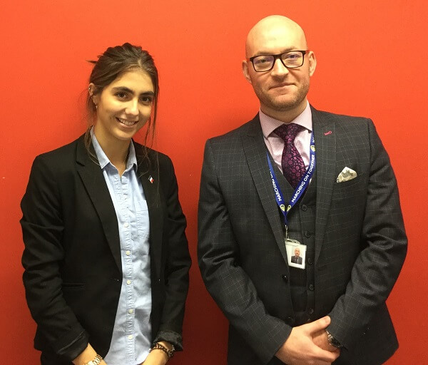 Pocklington School Sixth Form student and History teacher stood in front of orange wall.