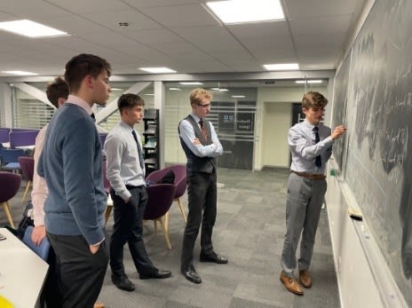 5 maths students doing calculations on classroom blackboard