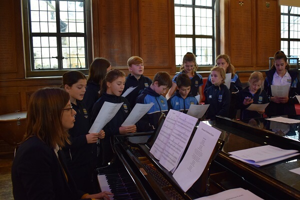 Children and teacher singing around a piano in Pocklington School Music Hall