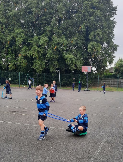 School boy pulling another boy along on a wheelie board in playground at Pocklington Prep School