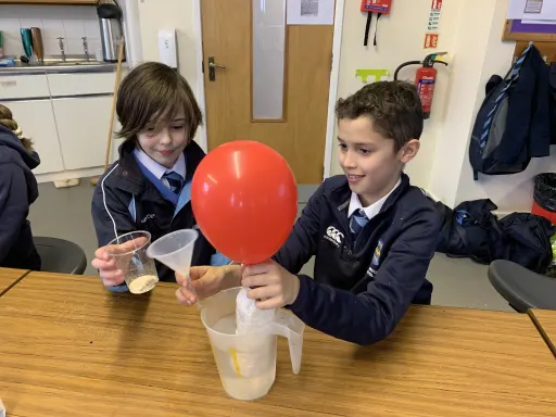 Two boys using water, yeast and sugar to inflate a red balloon in classroom